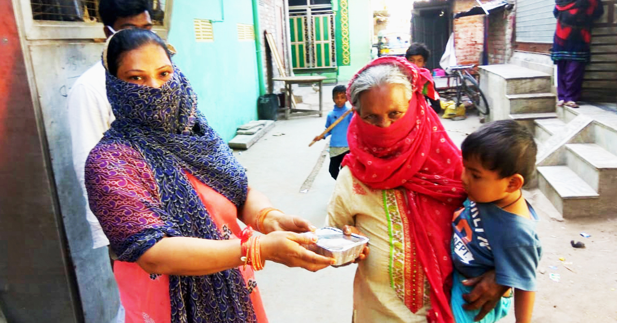 Indian woman with a scarf over her mouth and carrying a child accepts a package of food