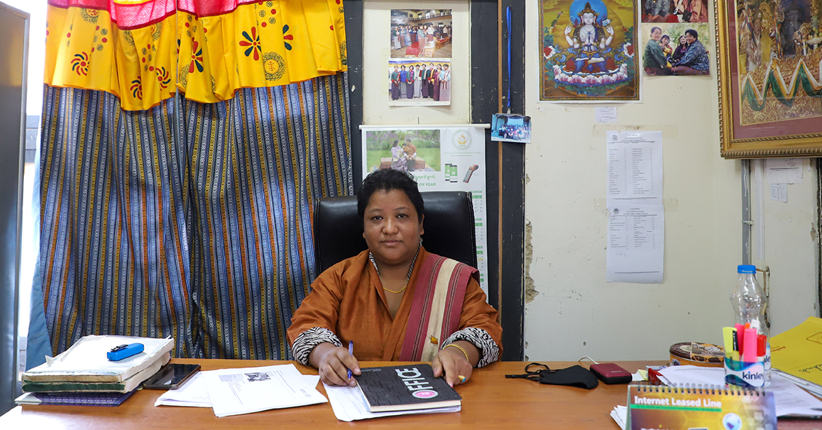 A Bhutanese woman is sitting at her work desk looking directly at the camera